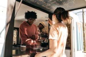 Proprietário de um food truck ajuda um cliente e anota um pedido de café usando um tablet digital.