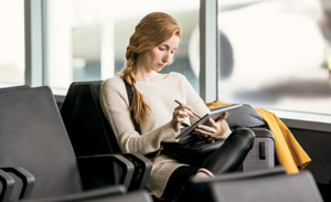 A woman sits in an airport working on her laptop.