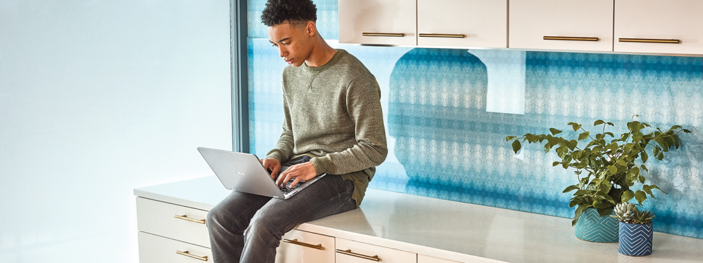 Image of a man sitting on a countertop with a laptop in his lap.